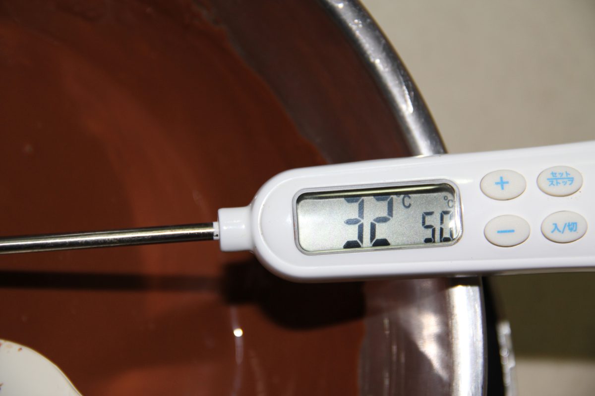 A thermometer reading 32C in melting milk-brown chocolate during tempering