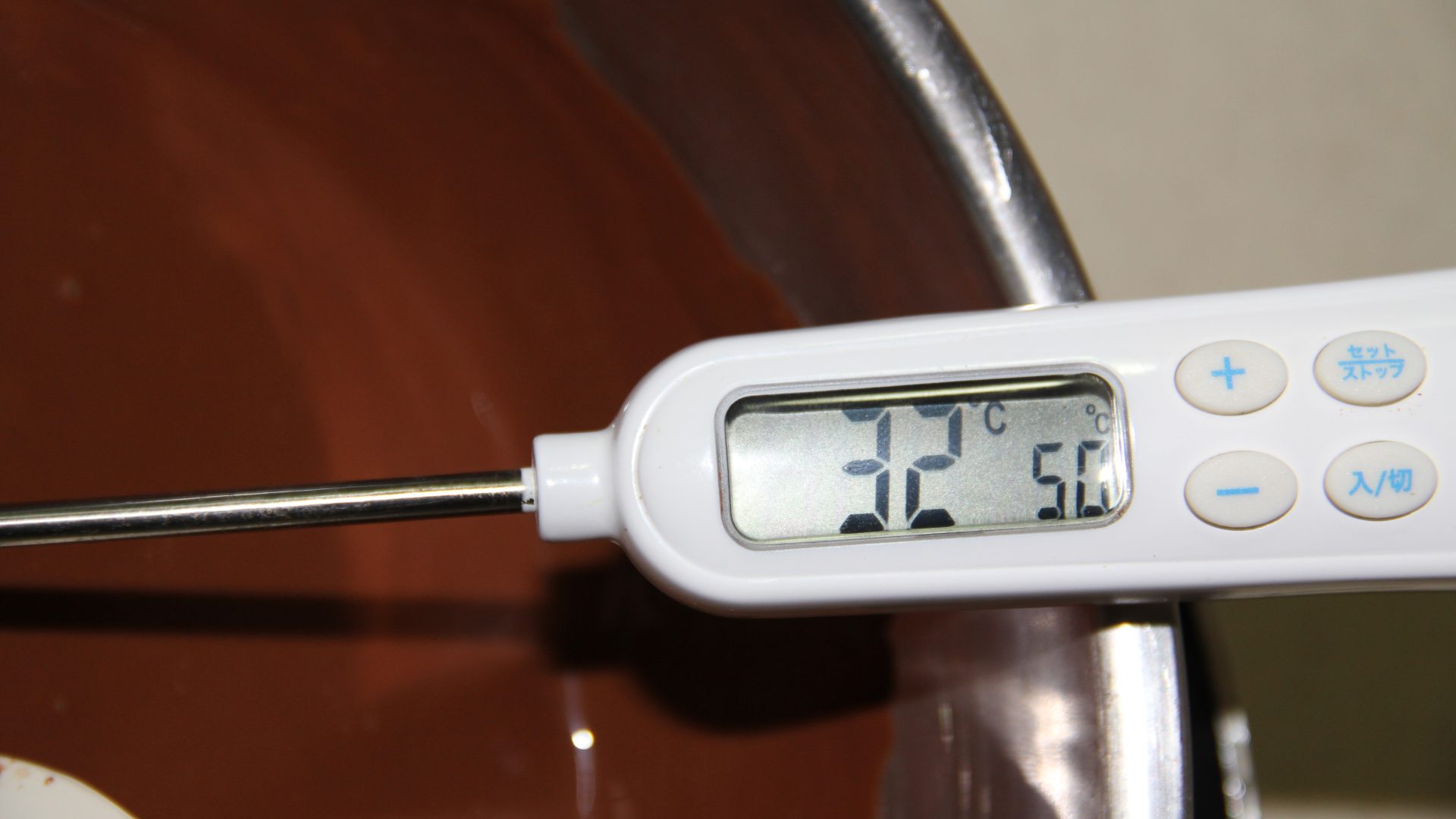A thermometer reading 32C in melting milk-brown chocolate during tempering
